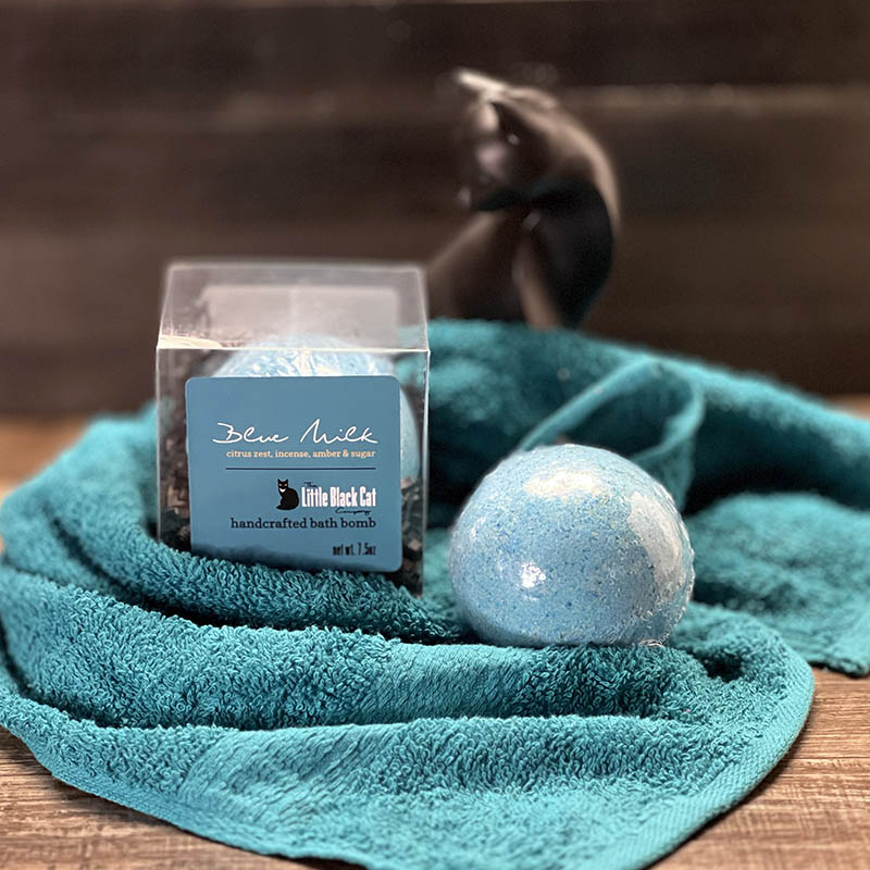 artistic arrangement of one boxed and one loose bath bomb with a towel and an art deco cat statue