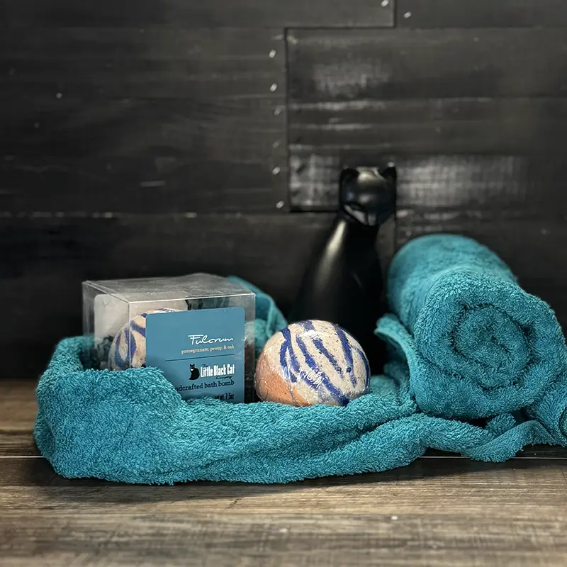 artistic arrangement of one boxed and one loose bath bomb with a towel and an art deco cat statue