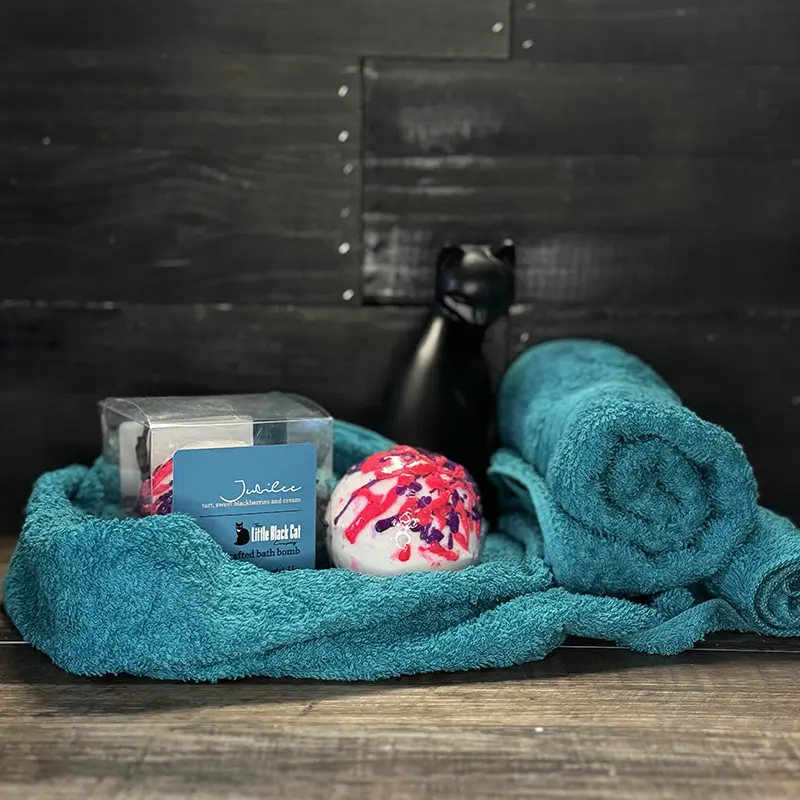 artistic arrangement of one boxed and one loose bath bomb with a towel and an art deco cat statue