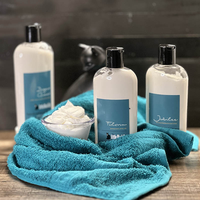an artistically arranged product photo of lotion bottles with a towel and a little cup of lotion displayed