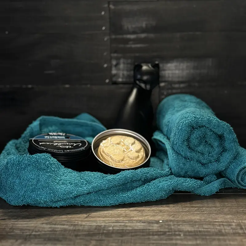 an artistically arranged product photo of lotion bottles with a towel and a little cup of lotion displayed
