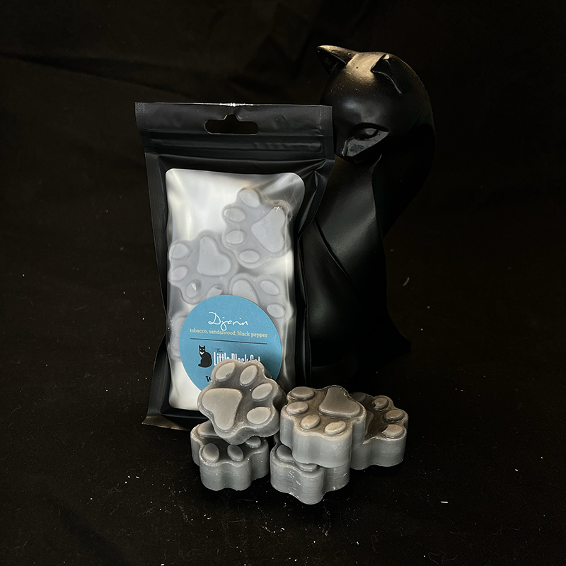 gray paw print shaped wax melts piled artfully in front of an art deco cat statue