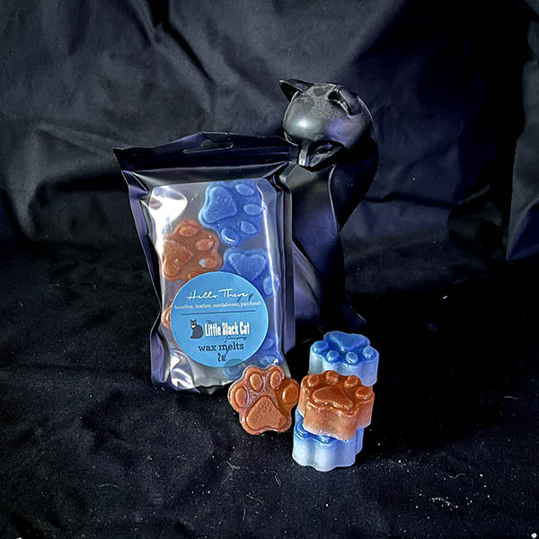 brown and blue paw print shaped wax melts piled artfully in front of an art deco cat statue
