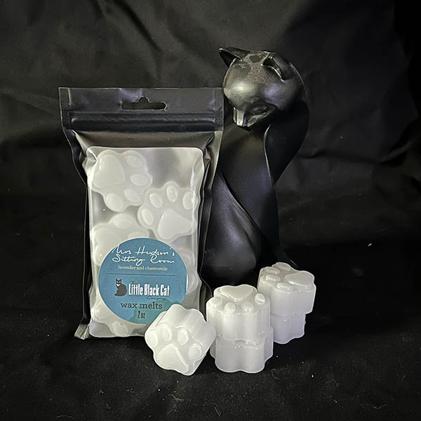 white paw print shaped wax melts piled artfully in front of an art deco cat statue