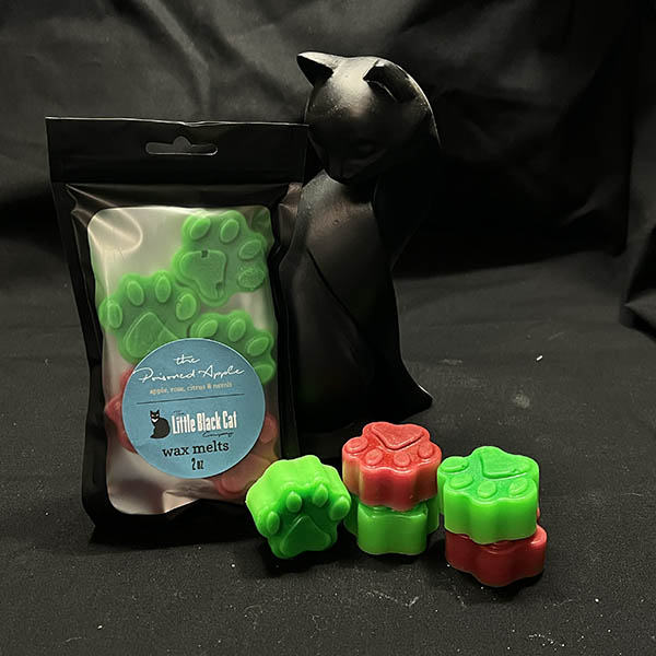 green and red paw print shaped wax melts piled artfully in front of an art deco cat statue