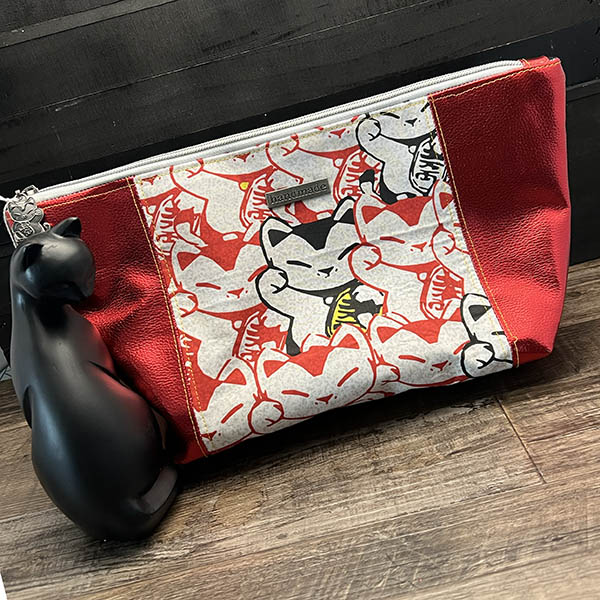 handmade cosmetics bag with red metallic vinyl and a pattern of lucky cats in red, black and white on a woven panel
