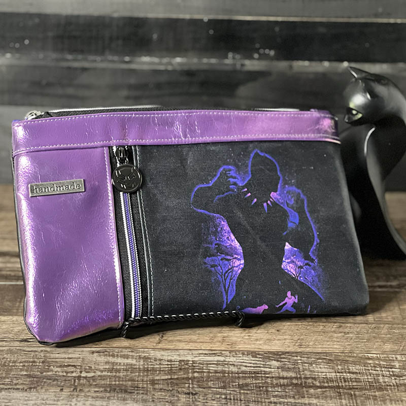 handmade zippy cluch with a fabric panel with a glowing silhouette design of a man in a panther costume, trimmed in metallic purple vinyl