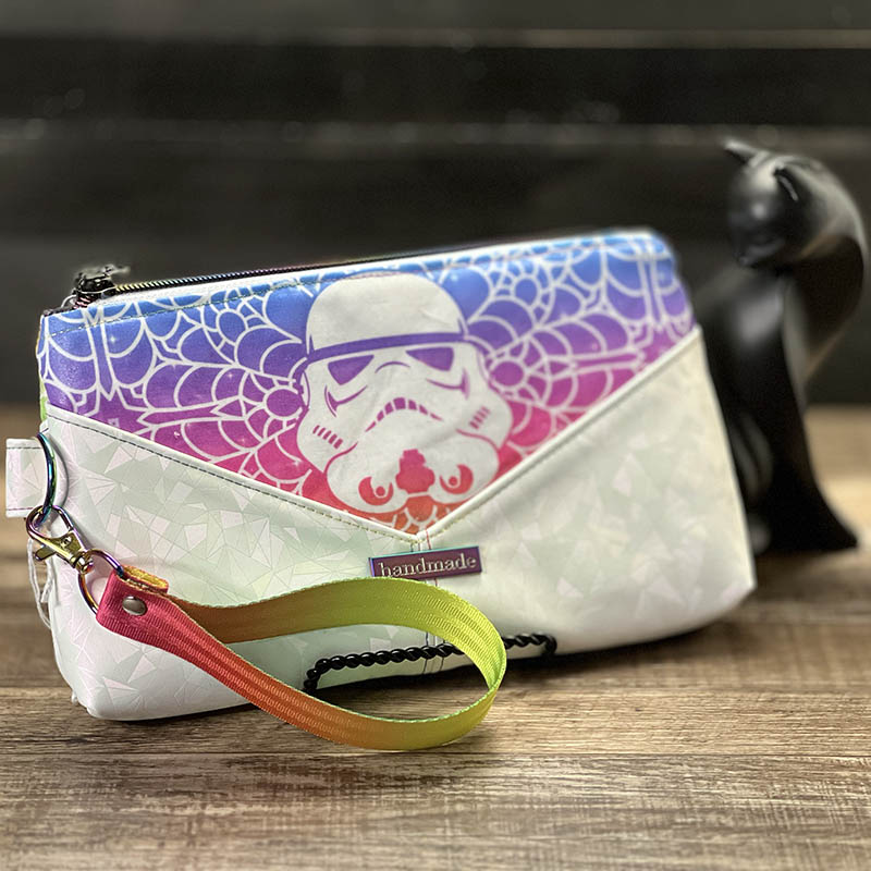 handmade wristlet done in cotton fabric and metallic white vinyl. Fabric design is a futuristic helmet surrounded by lace