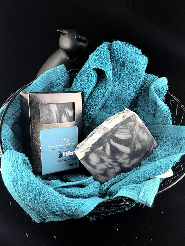 djarin soap bars, one in box one out, nested in a basket of teal towels with a sassy cat looking up at the viewer