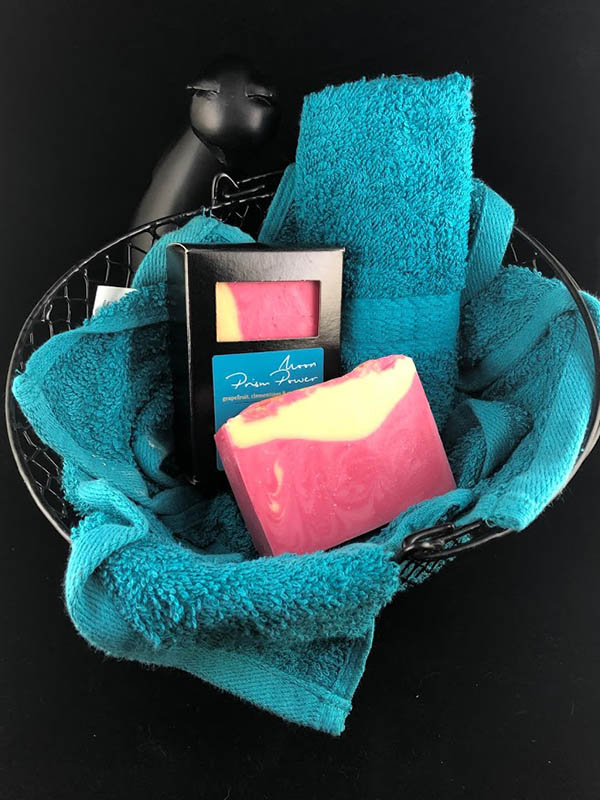 moon prism power soap bars, one in box one out, nested in a basket of teal towels with a sassy cat looking up at the viewer