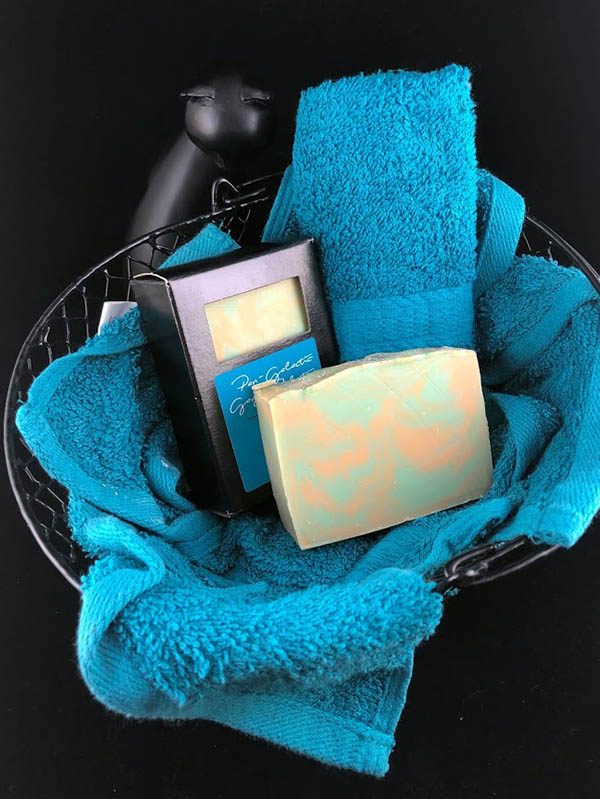 pan galactic gargle blaster soap bars, one in box one out, nested in a basket of teal towels with a sassy cat looking up at the viewer
