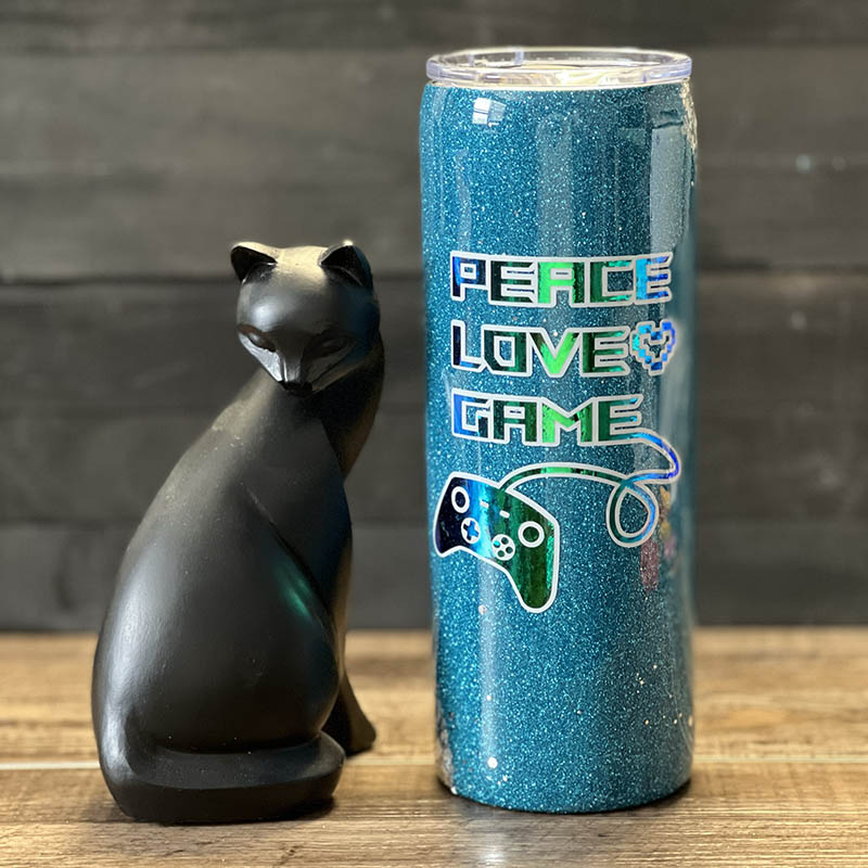 decorated 20oz steel tumbler with teal and silver glitter with a vinyl design that says peace love game