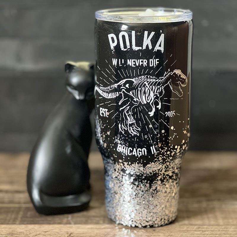 decorated 30oz steel tumbler done in black and silver glitter with a white vinyl t-rex skeleton design and the words polka will never die